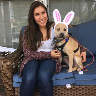 woman smiling next to her adopted dog who is wearing easter bunny ears